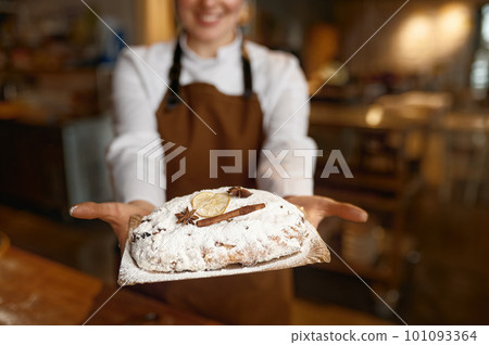 Young woman baker wearing uniform showing fresh bread closeup Young woman baker wearing uniform showing fresh bread closeup 101093364