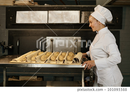 Baker pulling a tray with raw buns with sesame seeds prepared for baking 101093388