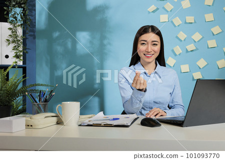 Joyful female employee at workplace showing good mood in front of the camera. Asian creative professional woman sitting in contemporary office making a korean heart gesture. 101093770
