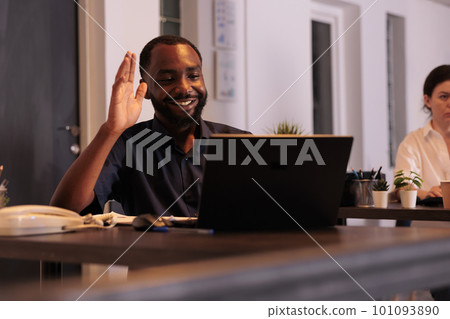 Smiling employee talking on videoconference with teamlead, waving hi, corporate worker answering teleconference call in office at night. African american man remote conversation in coworking space 101093890