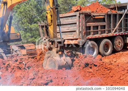 During construction process, an excavator is loading earth into dumper truck in order to transport it 101094048