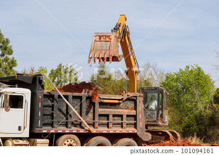 An excavator is loading earth into dumper heavy truck on construction site An excavator is loading earth into dumper heavy truck on construction site 101094161