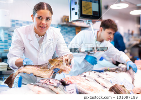 Positive saleswoman holding cod fish in fish store 101097189