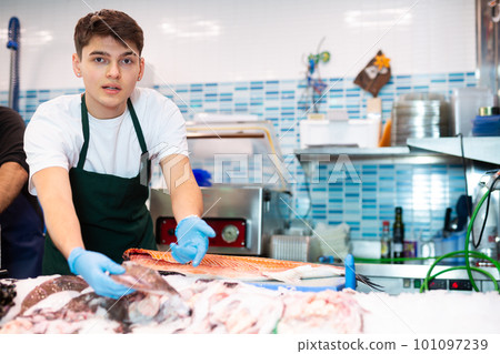 Positive salesman demonstrating sole fish behind counter in shop 101097239