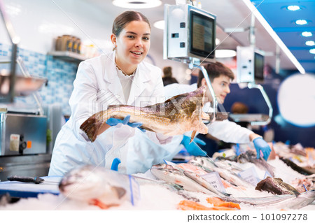 Positive saleswoman holding cod fish in fish store Positive saleswoman holding cod fish in fish store 101097278