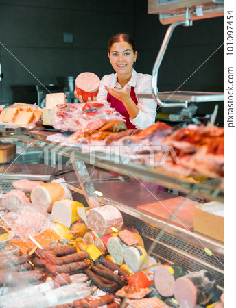 Smiling young girl seller offering fresh mortadella in grocery store 101097454