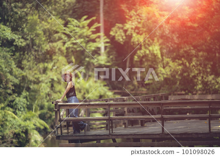 woman standing on wooden patio against deep green forest woman standing on wooden patio against deep green forest 101098026