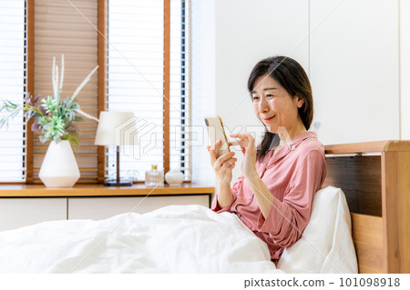 Woman in pajamas looking at smartphone in bed Woman in pajamas looking at smartphone in bed 101098918