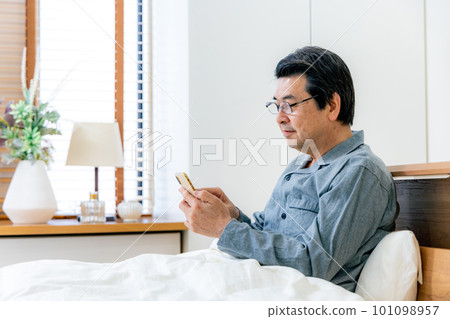 Middle-aged man using a smartphone in bed Middle-aged man using a smartphone in bed 101098957