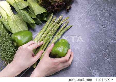 Female Hands Hold Assortment Of Fresh Organic Home Grown Green Vegetables On Granite Table. Asparagus Plant, Bell Pepper, Bok Choy, Red Leaf Lettuce, Bittercresses. Bio food.Horizontal, copy space. 101100327