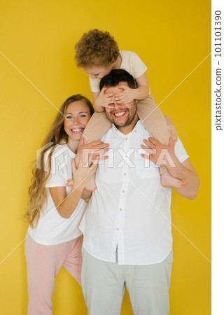 Portrait of a young happy family, parents hugging a child, son sitting on dad's neck on a yellow background. The concept of sincere emotions 101101390