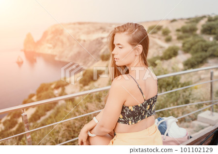 Woman travel sea. Happy tourist enjoy taking picture outdoors for memories. Woman traveler looks at the edge of the cliff on the sea bay of mountains, sharing travel adventure journey 101102129