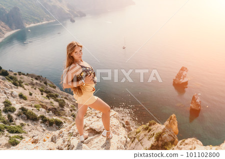 Woman travel sea. Happy tourist enjoy taking picture outdoors for memories. Woman traveler looks at the edge of the cliff on the sea bay of mountains, sharing travel adventure journey Woman travel sea. Happy tourist enjoy taking picture outdoors for memories. Woman traveler looks at the edge of the cliff on the sea bay of mountains, sharing travel adventure journey 101102800