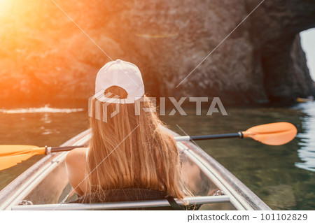 Woman in kayak back view. Happy young woman with long hair floating in transparent kayak on the crystal clear sea. Summer holiday vacation and cheerful female people relaxing having fun on the boat Woman in kayak back view. Happy young woman with long hair floating in transparent kayak on the crystal clear sea. Summer holiday vacation and cheerful female people relaxing having fun on the boat 101102829
