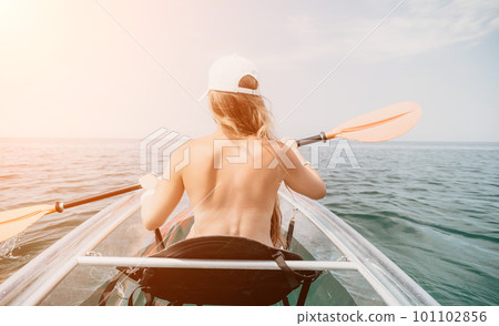 Woman in kayak back view. Happy young woman with long hair floating in transparent kayak on the crystal clear sea. Summer holiday vacation and cheerful female people relaxing having fun on the boat Woman in kayak back view. Happy young woman with long hair floating in transparent kayak on the crystal clear sea. Summer holiday vacation and cheerful female people relaxing having fun on the boat 101102856
