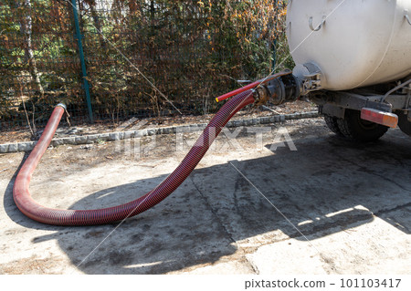 Close-up pipe hose of sewage truck car engine emptying home sewerage tank. Septic cleaning vacuum service and maintenance suburban countryside home. Suction vehicle cleaner machine pumping drainage Close-up pipe hose of sewage truck car engine emptying home sewerage tank. Septic cleaning vacuum service and maintenance suburban countryside home. Suction vehicle cleaner machine pumping drainage 101103417