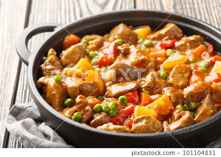 One pot of beef with potatoes, carrots, tomatoes, green peas, onions with spicy sauce close-up in a frying pan. Horizontal 101104831