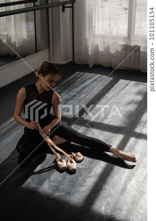 An Asian ballerina sits on the floor and puts on pointe shoes. 101105154