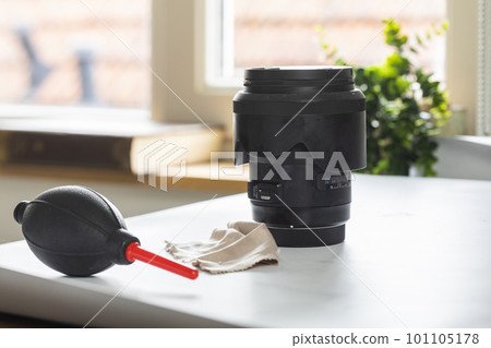 Lens on desk with cleaning tools for DSLR and Mirrorless cameras. Cleaning kit for cmos surface. Air blower, swab, isopropyl alcohol dropper and microfyber cloths. Lens and camera cleaning solution 101105178