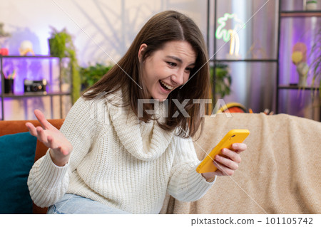 Happy young woman at home use smartphone typing browsing wow yes found out great big win celebrate 101105742