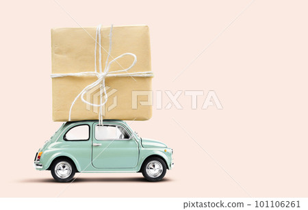 Retro toy car delivering gift box atop on a pale pink background 101106261