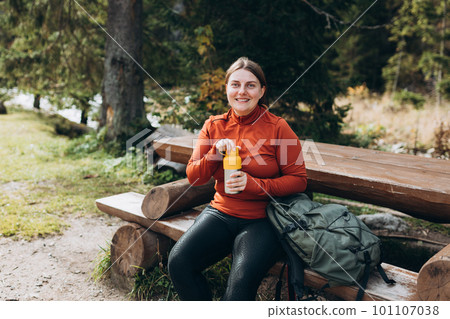 Happy redhead Woman in active trekking clothes having a halt after hiking. Hiker drinking water from water bottle or hot drink from yellow thermos Happy redhead Woman in active trekking clothes having a halt after hiking. Hiker drinking water from water bottle or hot drink from yellow thermos 101107038
