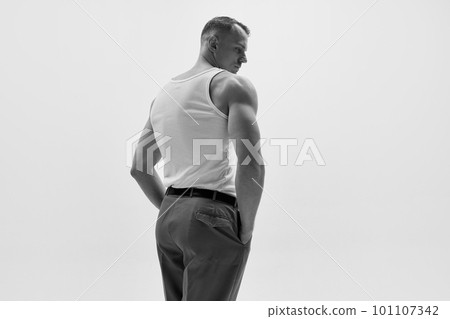 Portrait of muscular male fashion model wearing white t-shirt and posing over studio background 101107342