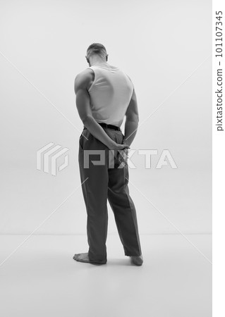 Studio shot of attractive man wearing classic trousers and posing over studio background. Muscular body shape. Monochrome 101107345