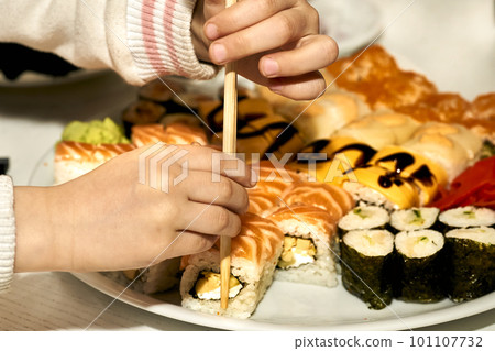 Children's hands taking delicious sushi with chopsticks. The child eats 101107732