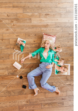Pretty attractive woman laying on wooden floor with cosmetics and magazines around her Pretty attractive woman laying on wooden floor with cosmetics and magazines around her 101108501