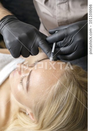 Doctor cosmetologist with syringe makes injection of botulinum toxin into forehead female patient in cosmetology clinic, beauty treatment in cosmetology. Vertical plane Doctor cosmetologist with syringe makes injection of botulinum toxin into forehead female patient in cosmetology clinic, beauty treatment in cosmetology. Vertical plane 101108666