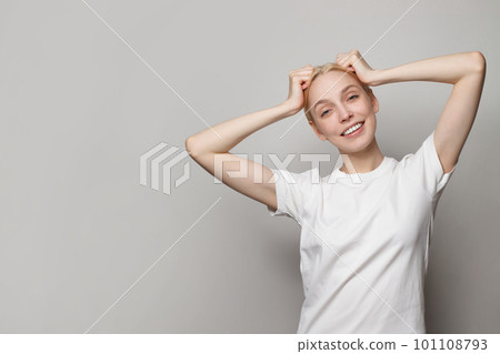 Joyful young woman wearing white empty t-shirt posing on grey studio background Joyful young woman wearing white empty t-shirt posing on grey studio background 101108793