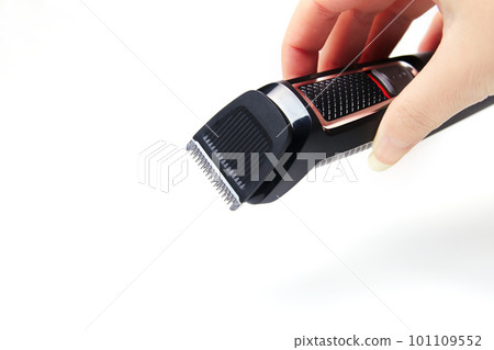 Professional hair clipper isolated on white background. Defocus female hand holding electric clipper on white background. Side view of the electric black hair clipper, closeup. Out of focus 101109552