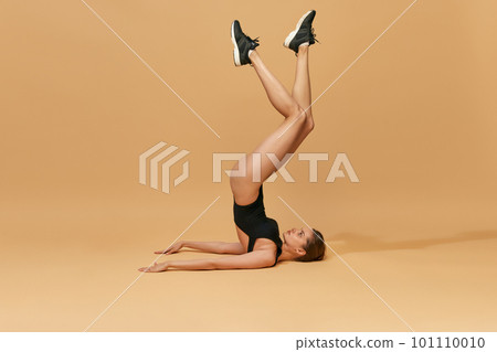 Athletic, beautiful, young girl with sportive strong body training in bodysuit against orange studio background. Flexibility Athletic, beautiful, young girl with sportive strong body training in bodysuit against orange studio background. Flexibility 101110010