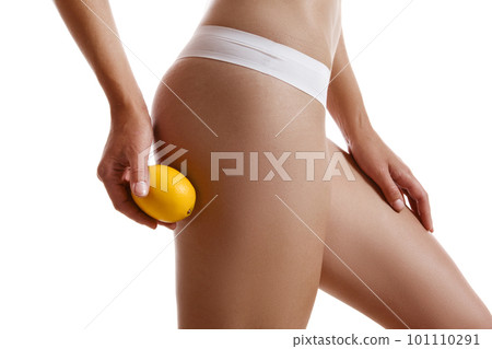 Perfect body of girl in white underwear touching her hip with lemon, isolated on white. Plastic surgery and aesthetic cosmetology concept. Close-up. 101110291