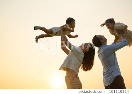 Father and mother holding children playing together in park in evening 101110324