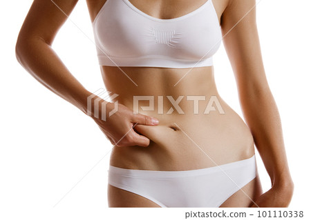 Young body of girl in white underwear, showing fat on her belly, posing isolated on white. Plastic surgery, aesthetic cosmetology concept. Close-up. 101110338