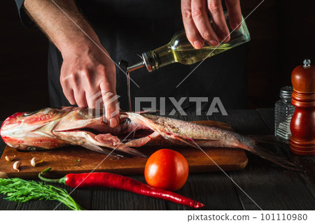 The chef prepares fresh fish bighead carp with add oil. Preparing to cook fish food. Working environment in restaurant or cafe kitchen 101110980