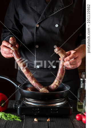 The cook puts raw meat sausage into the pan before cooking. Working environment in restaurant kitchen with vegetables and spices on the table 101110982