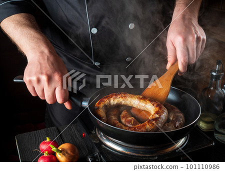 Cooking meat sausage in the restaurant kitchen. The chef fries sausage in frying pan. The idea of a delicious meat dish Cooking meat sausage in the restaurant kitchen. The chef fries sausage in frying pan. The idea of a delicious meat dish 101110986