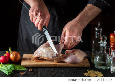 Preparing for cooking chicken legs in the restaurant kitchen. Chef cuts a chicken leg with a knife on cutting board 101110987