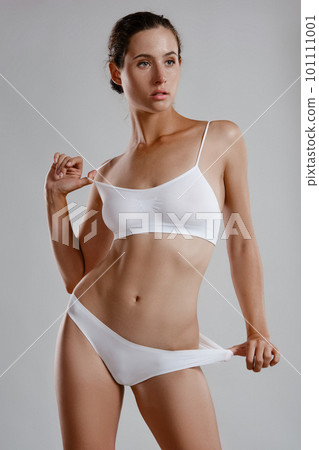 Perfect, slim, young body of a girl in white underwear posing against grey background. Plastic surgery and aesthetic cosmetology concept. Close-up. 101111001