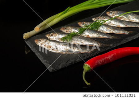 Sprat with vegetables on a serving board. Small salted fish with onion and pepper. Delicious dinner idea. 101111021