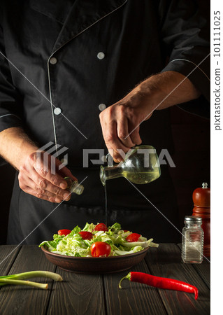 The chef pours olive oil into a bowl of salad. Cooking tasty and healthy food with set of vitamins The chef pours olive oil into a bowl of salad. Cooking tasty and healthy food with set of vitamins 101111025