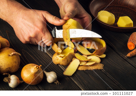Close-up cook hands are peeling raw potatoes with a knife for preparing a national dish or French fries. Delicious vegetable breakfast or lunch 101111027