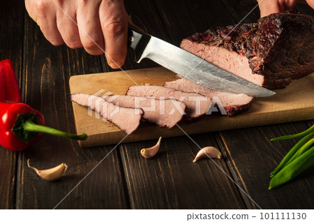 Slicing baked beef meat before preparing dinner by chef hands. Top view food preparation process concept Slicing baked beef meat before preparing dinner by chef hands. Top view food preparation process concept 101111130