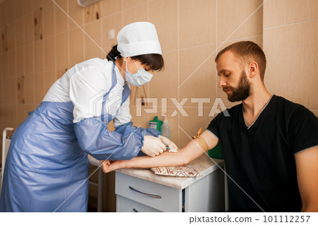 Doctor woman in a white robe makes an injection to a young man in the treatment room of the hospital. 101112257