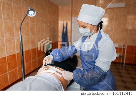 Woman doctor in a protective mask in a medical uniform puts a bandage over the wound in a hospital. A nurse cares for a sick patient. Back injury Woman doctor in a protective mask in a medical uniform puts a bandage over the wound in a hospital. A nurse cares for a sick patient. Back injury 101112415