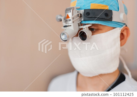 microsurgeon man in a white mask in special medical clothes and glasses with binocular loupes in the operating room. surgeon makes an operation. Hospital equipment microsurgeon man in a white mask in special medical clothes and glasses with binocular loupes in the operating room. surgeon makes an operation. Hospital equipment 101112425