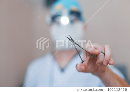Surgeon in special medical clothes holds surgical metal scissors in his hand. Focus on the instrument. Operation process Close-up. Surgeon in special medical clothes holds surgical metal scissors in his hand. Focus on the instrument. Operation process Close-up. 101112436
